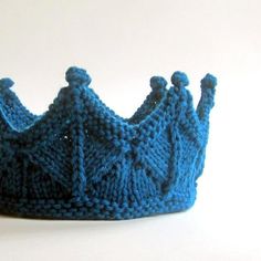 a knitted blue crown sitting on top of a white table next to a wall