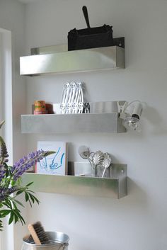 two metal shelves with utensils and other kitchen items on them in a white room