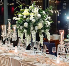 the centerpieces on this table are all white and have flowers, candles, and greenery