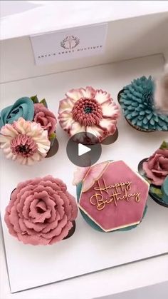 cupcakes decorated with pink, blue and white flowers are displayed in a box