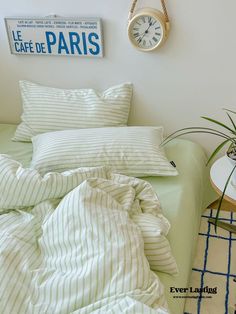 a bed with white and green striped comforter next to a clock on the wall