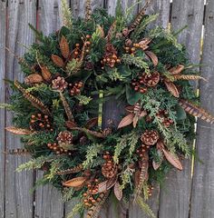 a wreath with pine cones and evergreens hanging on a wooden fence next to some plants