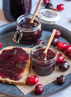 two jars of jam sit on a plate with bread and cherries