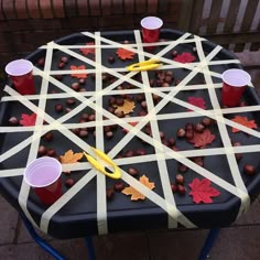 an outdoor game made out of sticks and plastic cups with fall leaves on them, sitting on a table