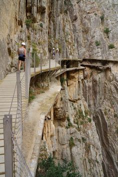 a man standing on top of a wooden bridge over a river next to a cliff