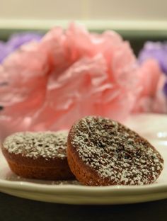 two powdered donuts on a white plate next to a pink tissue paper flower