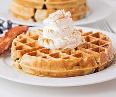 two plates with waffles, bacon and whipped cream sitting on top of them