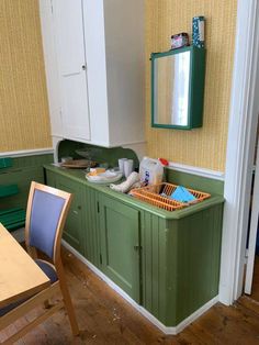 a kitchen with green cabinets and white cupboards next to a wooden table in front of a mirror