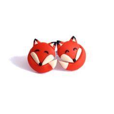 two red fox earrings with black ears and white tails on them, sitting side by side in front of a white background