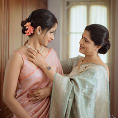 two women standing next to each other in front of a wooden wall and one is adjusting the collar of another woman's neck