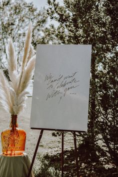 an easel with a sign and some feathers on it next to a tree in the background