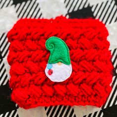 a crocheted red and white square with a green gnome hat on it's side