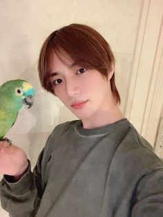 a young man holding a green and yellow parakeet on his arm in front of a mirror