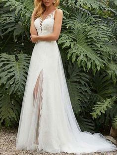 a woman standing in front of some plants wearing a white wedding dress with high slit