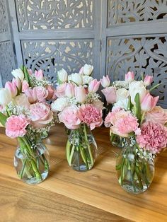 three vases filled with pink and white flowers on top of a wooden table next to a wall