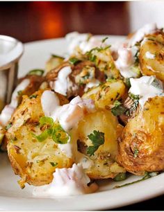 a white plate topped with potatoes covered in sour cream and garnished with herbs