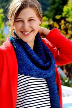 a woman wearing a red cardigan, striped shirt and blue scarf smiles at the camera