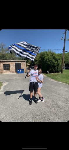 a man and woman holding an american flag in the middle of a road with a building behind them