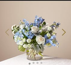 a glass vase filled with blue and white flowers on top of a table next to a wall