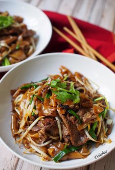 two white bowls filled with beef and noodles on top of a wooden table next to chopsticks