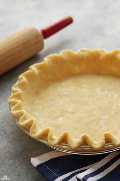 an uncooked pie crust sits on a table next to a rolling pin