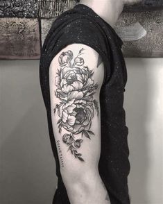 a man with a black and white flower tattoo on his arm, standing in front of a wall