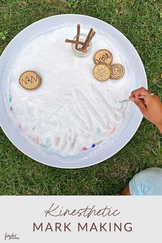 a child's hand is painting the letters on a paper plate with cookies and marshmallows