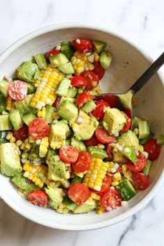 a white bowl filled with corn, avocado and tomato salad on top of a marble counter