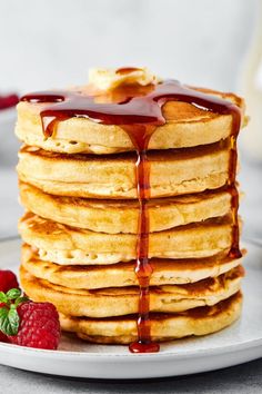 stack of pancakes covered in syrup and drizzled with strawberries on the side