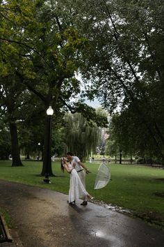 a man and woman kissing in the rain under umbrellas on a path near trees