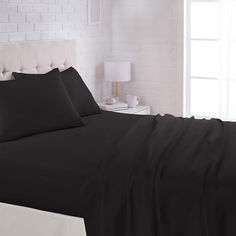 a bed with black sheets and pillows in a white room next to a brick wall