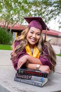 a girl in graduation cap and gown leaning on two books with her arms folded out