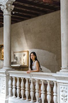 a beautiful young woman standing on top of a white balcony next to a painting hanging on the wall