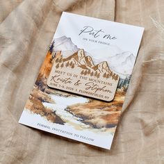 a card with a mountain scene on it sitting on top of a bed sheet in front of a pillow