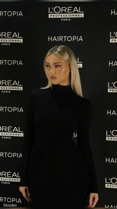 a woman standing in front of a black backdrop wearing a dress with high neck and long sleeves