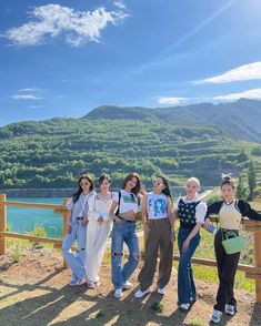 four girls standing on a hill overlooking a lake and mountains in the background, with one girl holding a green purse