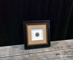 a small brown and black frame with a flower in it on a wooden table next to a black wall