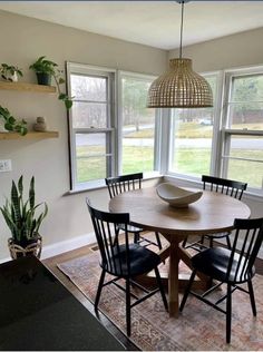 a dining room table with four chairs and a bowl on top of it in front of two windows