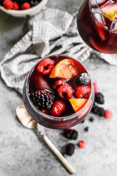 two glasses filled with fruit and ice on top of a gray table next to silver spoons