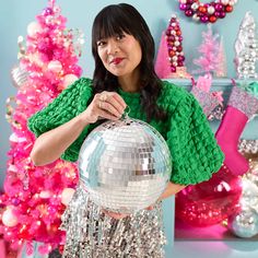 a woman holding a disco ball in front of a christmas tree with pink and green decorations