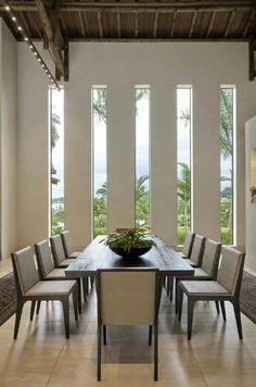 a dining room table with chairs and a plant in the center surrounded by large windows