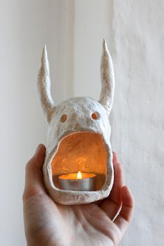 a hand holding a candle holder with a white animal head on it's face