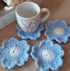 four crocheted flower coasters sitting on a table next to a coffee cup