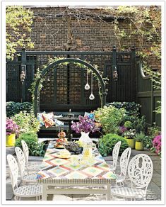 an outdoor dining area with white chairs and table surrounded by plants, flowers and potted plants