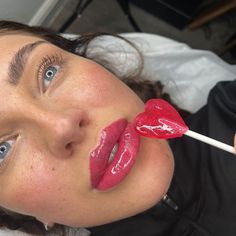 a woman with blue eyes holding a red heart shaped lollipop in her mouth