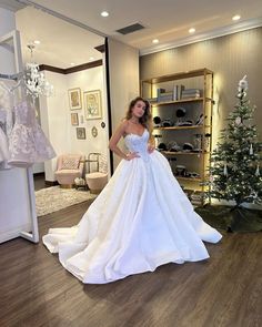 a woman standing in front of a christmas tree wearing a white wedding dress and looking at the camera