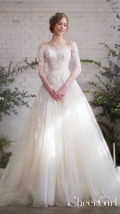 a woman in a wedding dress standing next to a white brick wall with greenery