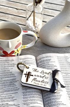 an open book with a cross on it next to a cup of coffee