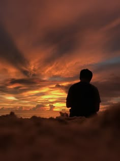 a man sitting on top of a sandy beach under a cloudy sky