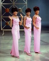 three women in pink dresses standing next to each other on a tv set with one holding her hand up